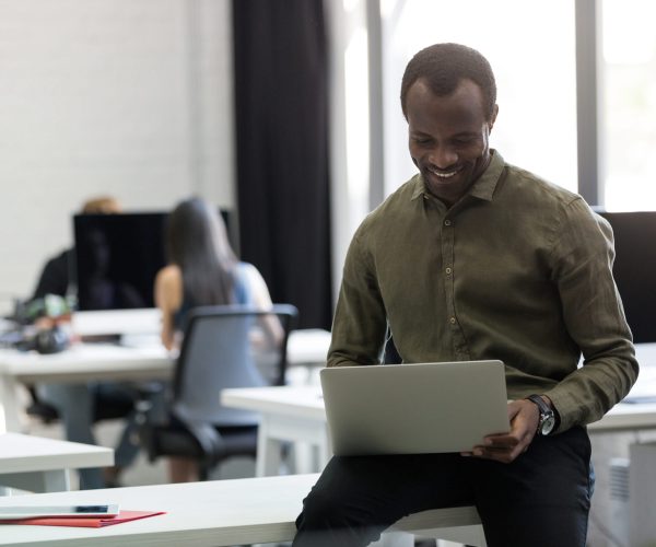 Happy afro american businessman sitting on his desk and typing on laptop computer in an office